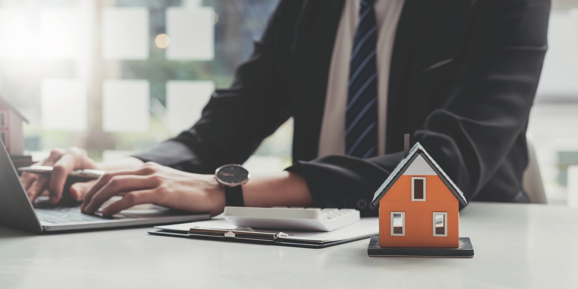 Photo of a house model putting on a clipboard at the wooden working desk over a real estate using a