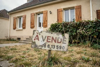 Panneau à vendre mal entretenu avec lettrage effacé devant une maison en vente aux volets fermés